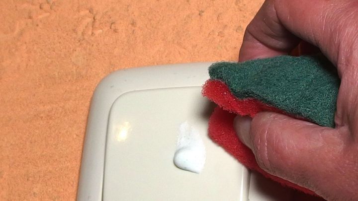 Eine Hand hält ein Reinigungstuch, das mit Zahnpasta über weißes Plastik gewischt wird, um es zu säubern.