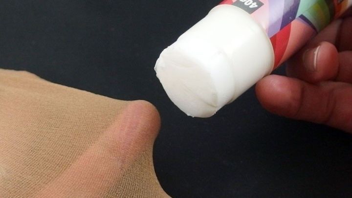 Ein Klebestift wird auf eine Nylonstrumpfhose aufgetragen, um eine Laufmasche zu reparieren, in einem neutralen Umfeld.