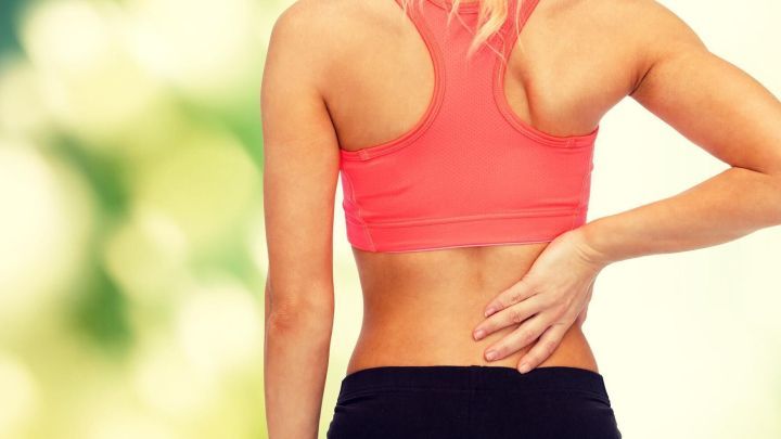 Eine Person mit R&uuml;ckenschmerzen h&auml;lt sich den unteren R&uuml;cken, w&auml;hrend sie in einem hellen, nat&uuml;rlichen Umfeld steht.