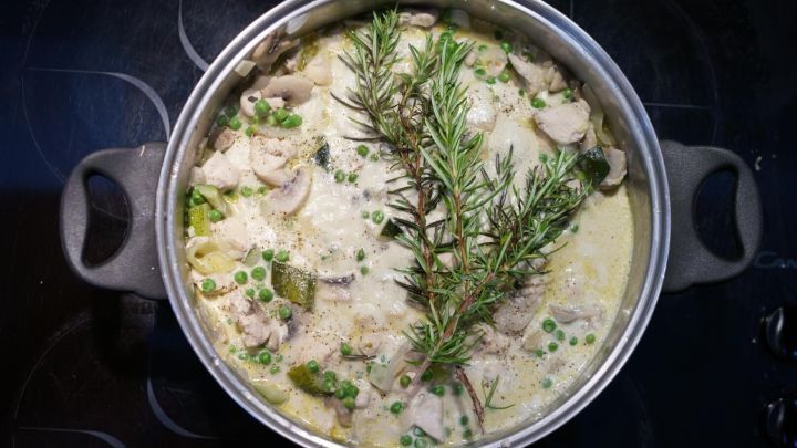 Ein Topf mit Huhn und Gem&uuml;se wird auf dem Herd gekocht, garniert mit frischem Rosmarin f&uuml;r zus&auml;tzlichen Geschmack.