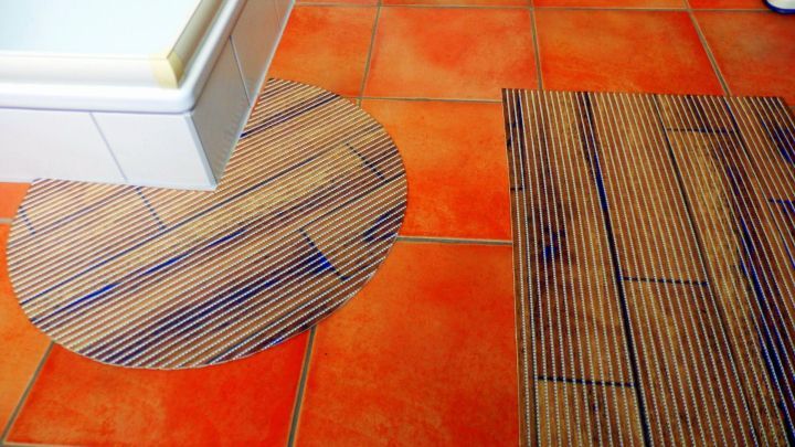 Badematten: Eine runde und eine rechteckige Matte liegen auf roten Fliesen neben einer wei&szlig;en Badewanne.