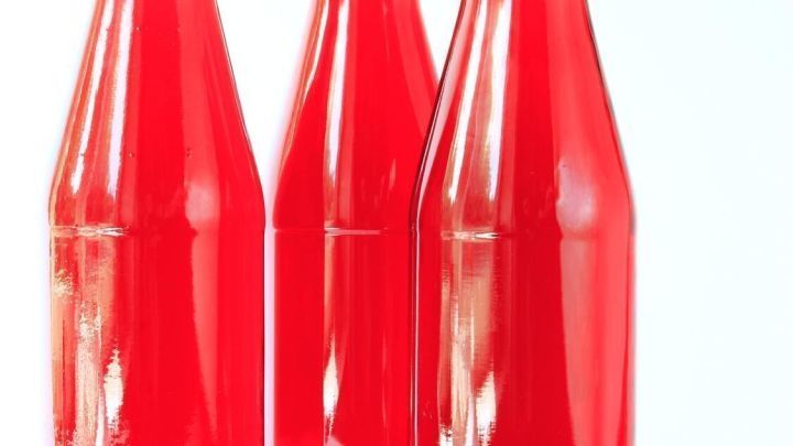 Drei Glasflaschen mit rotem Erdbeerwein stehen auf einem wei&szlig;en Hintergrund, dekoriert mit karierten Deckeln.