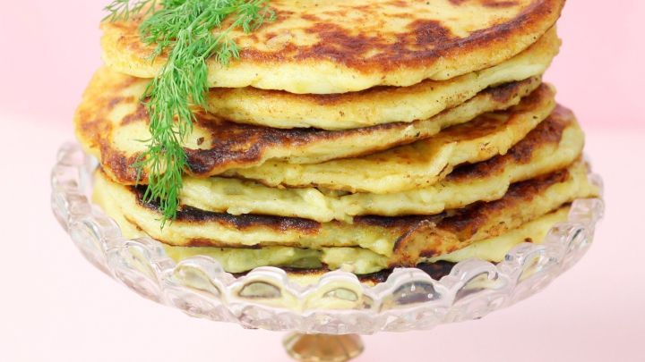 Ein Stapel knuspriger Stampfkartoffelgerichte steht auf einem eleganten Glasteller, dekoriert mit frischem Dill.