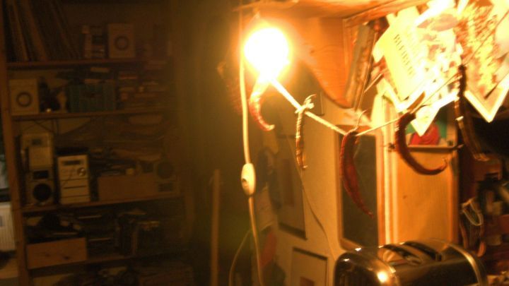 Eine gl&uuml;hende Lampe h&auml;ngt in einem Raum voller B&uuml;cher und Notizen, die zur Nachbarschaftshilfe einladen.