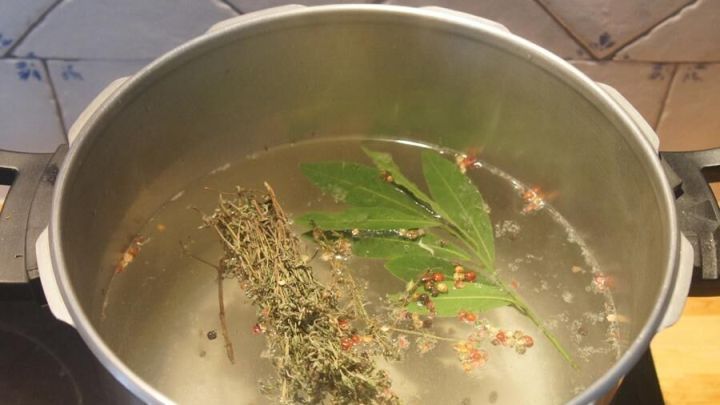 Ein gro&szlig;er Topf mit Kr&auml;utersud kocht, w&auml;hrend frische Kr&auml;uter im Wasser schwimmen, bereit f&uuml;r die Taschenkrebse.