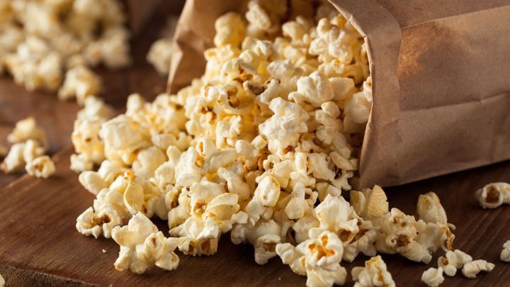 Popcorn liegt verstreut auf einem Tisch, aus einer papiernen Verpackung herausfallend, bereit f&uuml;r einen snackigen Genuss.