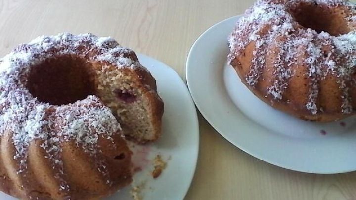 Zwei Gugelhupfs aus Kokos und Kirsche stehen auf Tellern, einer ist angeschnitten und mit Puderzucker bestreut.