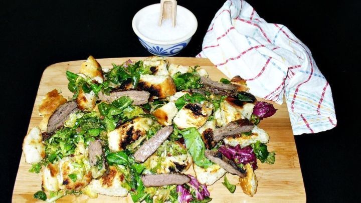 Saftige Steakstreifen liegen auf einem bunten Wildgem&uuml;sesalat, umgeben von krossem Fladenbrot und einer Schale Salz.