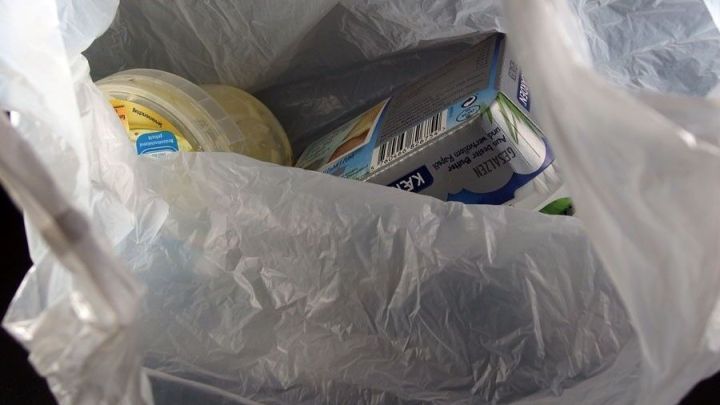 Eine durchsichtige M&uuml;llt&uuml;te enth&auml;lt verschiedene Lebensmittelverpackungen, die als Abfall in einem Einkaufsumfeld zu sehen sind.