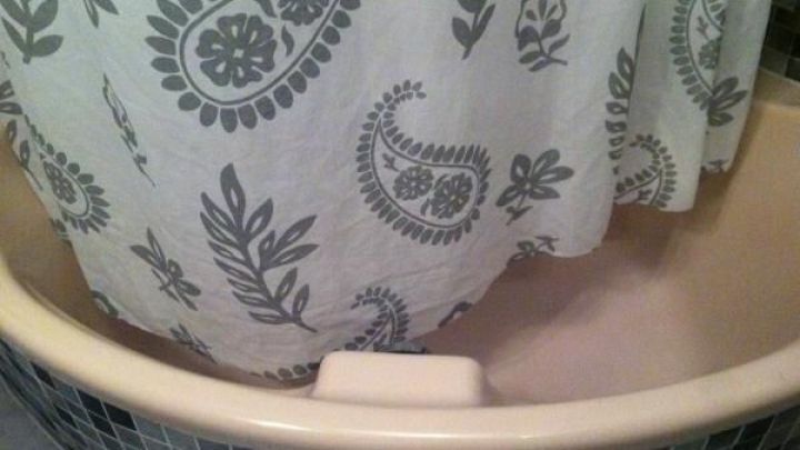 Ein Duschvorhang mit floralem Muster h&auml;ngt in einer Badewanne, umgeben von dunklen Fliesen.