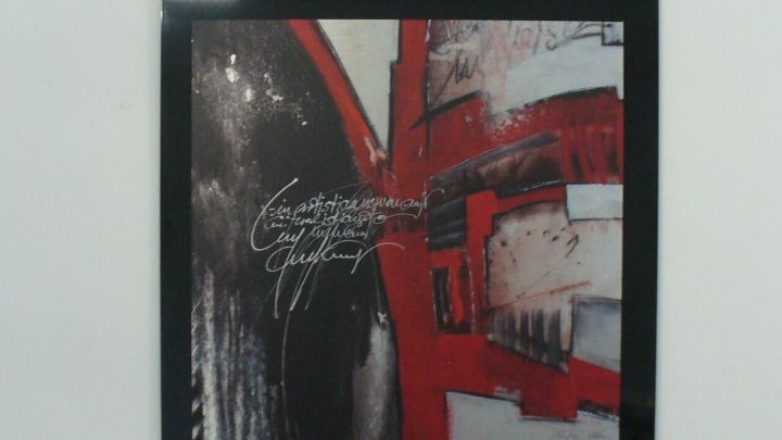 Ein schwarzer Bilderrahmen mit einer k&uuml;nstlerischen Collage ist an der Wand aufgeh&auml;ngt und zeigt lebhafte Farben.