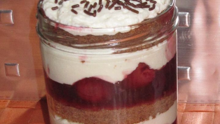 Schwarzw&auml;lder Kirschtorte im Glas mit Sahnehaube, Kirsche und Schokoladenstreuseln auf einem Tisch; Text: Bild von Tastenmaus.