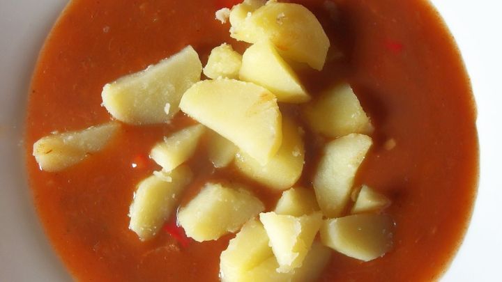 Eine Sch&uuml;ssel mit Suppe enth&auml;lt geviertelte Kartoffeln, die in einer tomatigen Fl&uuml;ssigkeit schwimmen, auf einem wei&szlig;en Tisch.