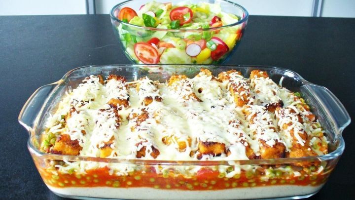 Ein frisch gebackener Fischst&auml;bchen Auflauf liegt in einer Glasform, umgeben von einer bunten Salatsch&uuml;ssel.