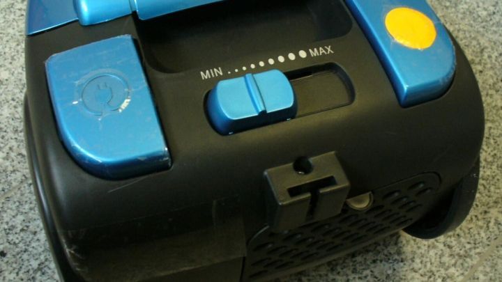 Staubsauger mit blauer Steuerung auf grauem Boden, zeigt Regler f&uuml;r "MIN...MAX".