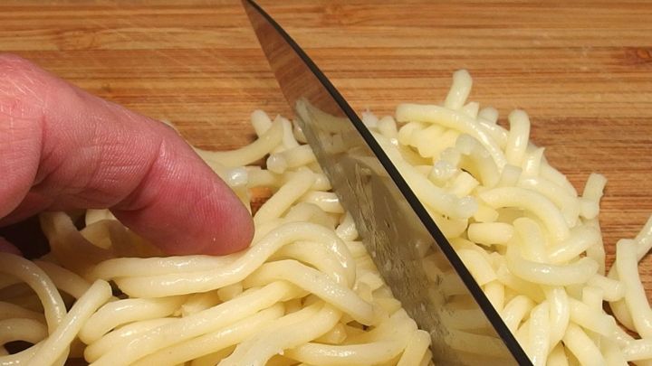 Spaghetti werden mit einem Messer auf einem Holzbrett in kleinere St&uuml;cke geschnitten, um Reste sinnvoll zu verwerten.