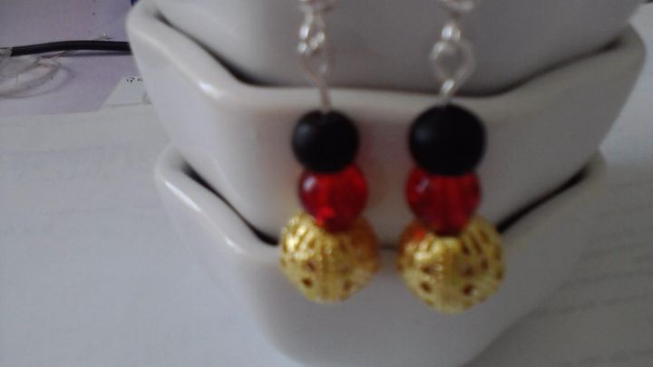 Bunte Ohrringe h&auml;ngen an einem silbernen Haken, auf einem wei&szlig;en Teller in einem hellen Raum arrangiert.