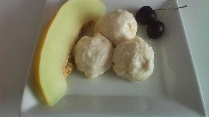 Drei Kugeln Pina Colada Eis liegen auf einem wei&szlig;en Teller, dekoriert mit einer Melonenscheibe und zwei Kirschen.