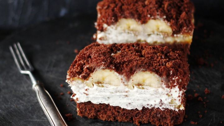 Saftiger Maulwurfkuchen vom Blech mit einer Schicht Bananen und Sahne, auf einem dunklen Hintergrund angerichtet.