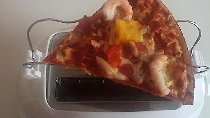 Ein Pizzast&uuml;ck wird auf einem Toaster knusprig aufgebacken; es liegt auf einer Metallhalterung im hellen Raum.