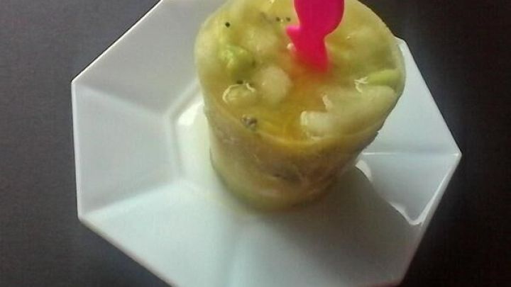 Ein rundes Fruchteis aus Honigmelone und Kiwi steht auf einem achteckigen wei&szlig;en Teller, verziert mit einem pinken Stiel.