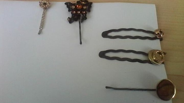 Verschiedene Haarklammern mit individuellen Verzierungen liegen auf wei&szlig;em Papier auf einem Holztisch.