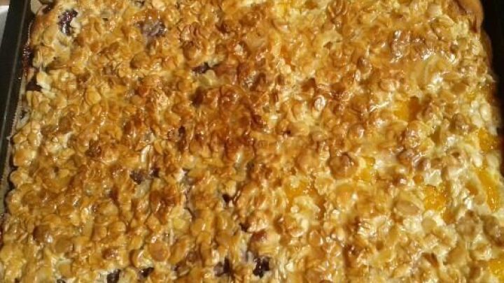 Ein Obstkuchen vom Blech, goldbraun gebacken und mit Fr&uuml;chten belegt, ruht auf einem mit Backpapier ausgelegten Blech.