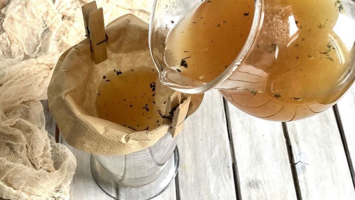 Eine transparente Kanne gie&szlig;t eine goldene Fl&uuml;ssigkeit durch einen Filter in ein Gef&auml;&szlig;, um So&szlig;en abzu-seihen.