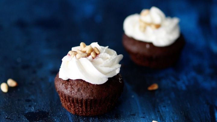 Schokoladenmuffins mit einer cremigen Dekoration und Pinienkernen auf einem blauen Hintergrund stehen appetitlich.