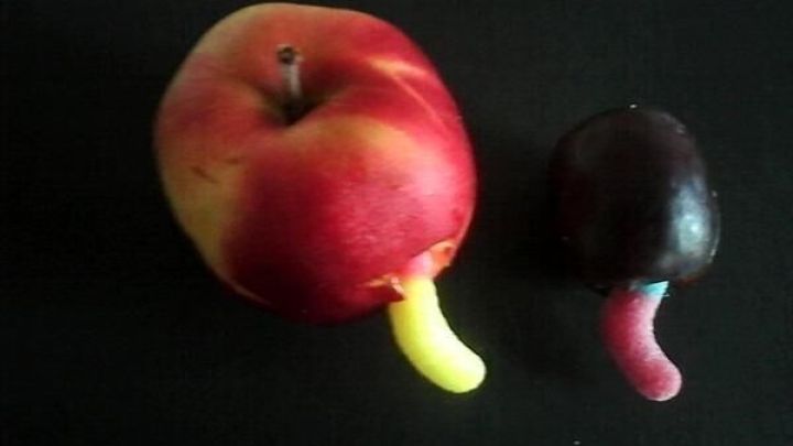 Ein roter Apfel und eine Traube mit Gummiw&uuml;rmern im schwarzen Hintergrund, die f&uuml;r Kinder dekoriert sind.