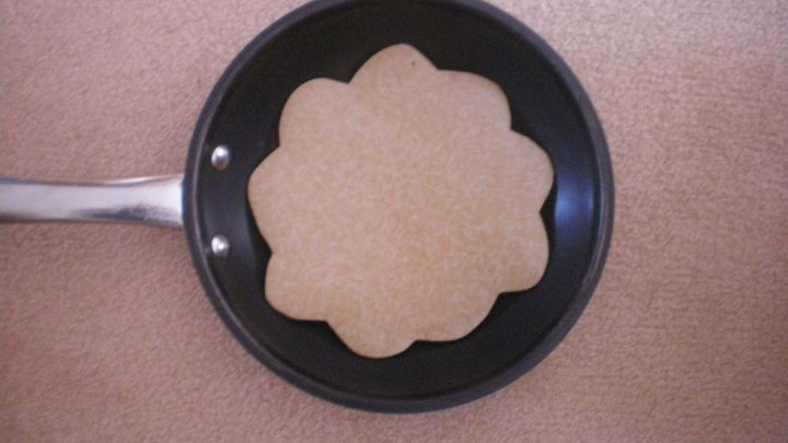 Eine runde Pfannenschutzeinlage liegt in einer schwarzen Pfanne auf einem hellen Untergrund und sch&uuml;tzt die Pfanne.