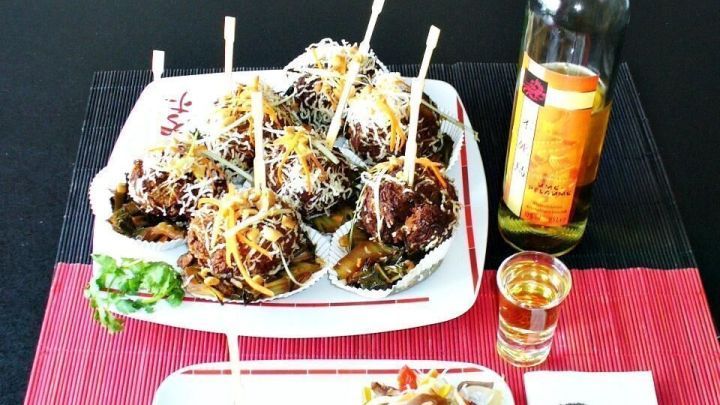 Asiatische Hackb&auml;llchen in Glasnudelpanade liegen appetitlich auf Tellern, umgeben von Dekoration und einem Getr&auml;nk.