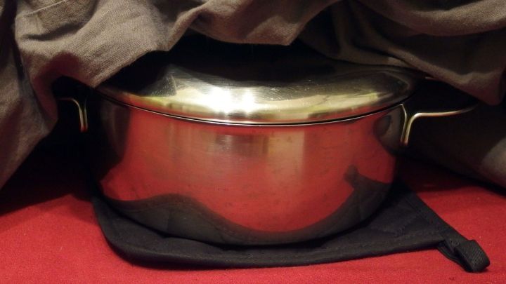 Ein edelstahlener Topf h&auml;lt Kartoffeln warm, w&auml;hrend ein dunkles Tuch dar&uuml;ber liegt. Der Topf steht auf einem schwarzen Untersetzer.