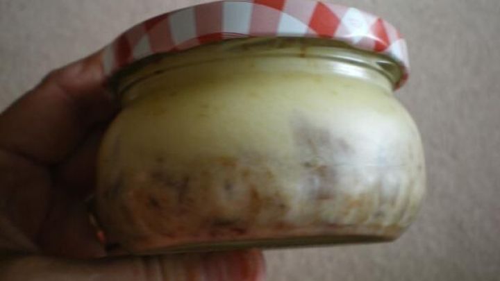 Ein Glas mit Schmalz wird von einer Hand gehalten. Es hat einen rot-wei&szlig;en karierte Deckel, im Hintergrund ein Teppich.