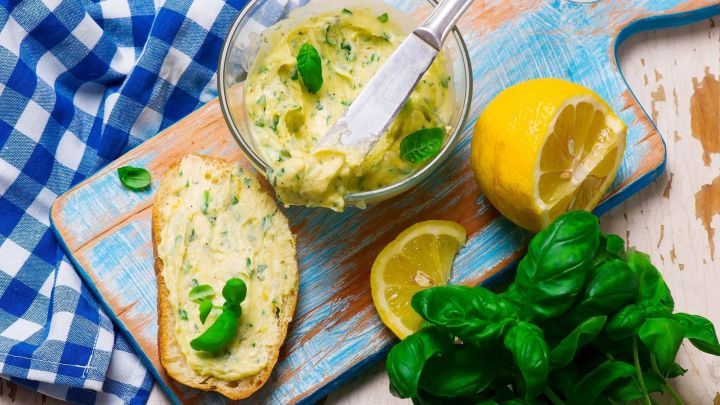 Eine Sch&uuml;ssel mit Zitronenbutter steht auf einem Holzbrett, daneben frisches Basilikum und Zitronenscheiben.