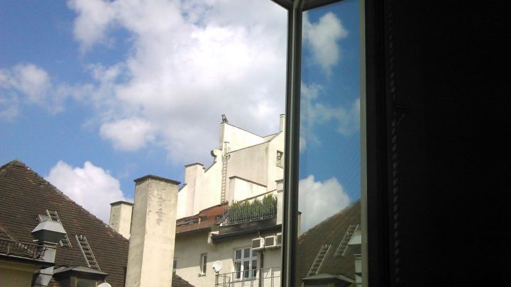 Ein offenes Fenster reflektiert den blauen Himmel und Wolken, w&auml;hrend die Wohnung im Schatten bleibt.