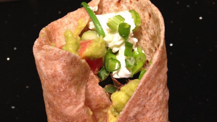 Ein Wrap aus Vollkorn, gef&uuml;llt mit Avocado und Ziegenk&auml;se, auf einem schwarzen Untergrund pr&auml;sentiert.