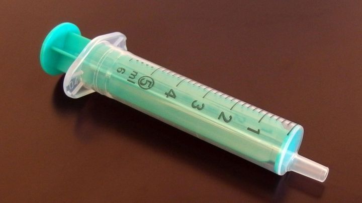 Eine Spritze mit gr&uuml;ner Fl&uuml;ssigkeit liegt auf einer glatten, dunklen Oberfl&auml;che, bereit zum Aussaugen von Pickeln.