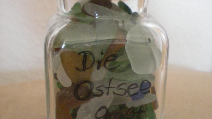 Ein Glasbeh&auml;lter mit Meerglas gef&uuml;llt, beschriftet mit "Die Ostsee gr&uuml;&szlig;t Moni." Ein lustiger Sonnensymbol-Aufkleber schm&uuml;ckt es.