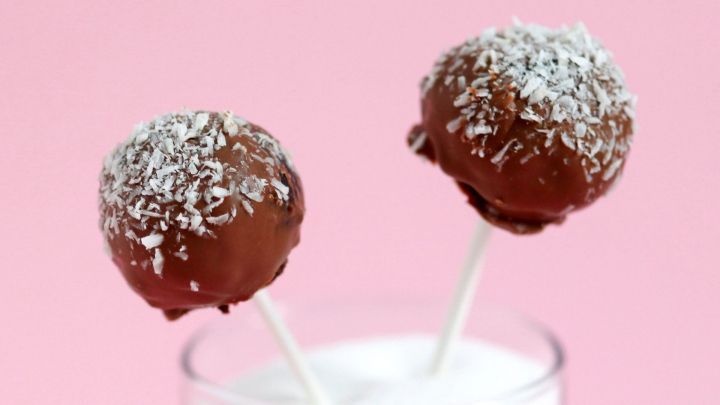 Schokoladenkuchen-Lollis stecken auf Schaschlikspie&szlig;en in einem Glas mit Zucker, vor einem rosa Hintergrund.