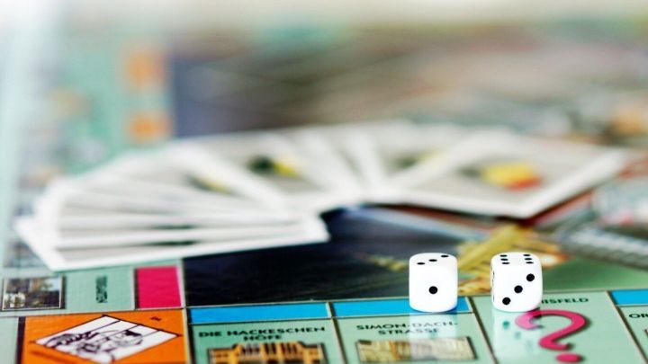 Auf einem Spiele-Tisch liegt ein Monopoly-Spielbrett mit W&uuml;rfeln und Karten, w&auml;hrend ein Kind frustriert reagiert.