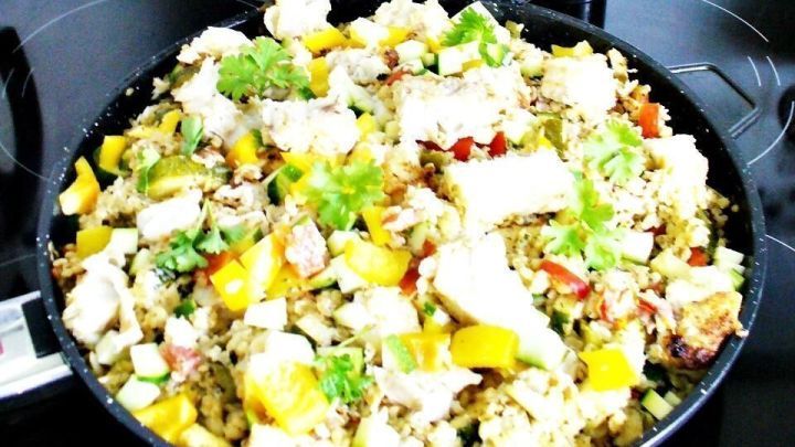 Eine bunte Pfanne mit Kabeljau, Bulgur, Zucchini und Paprika wird auf einem Herd in einer modernen K&uuml;che zubereitet.