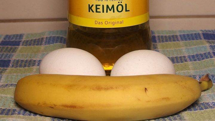 Eine Banane liegt auf einem karierten Tuch, w&auml;hrend zwei Eier und eine Flasche Bananen-&Ouml;l im Hintergrund stehen.