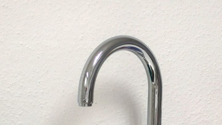 Ein gl&auml;nzender Wasserhahn wird gegen Kalk behandelt, der sich auf der Oberfl&auml;che abgesetzt hat, vor einer neutralen Wand.