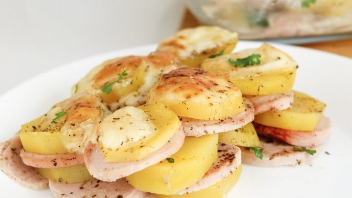 Ein geschichteter Auflauf aus Fleischwurst und Kartoffeln, &uuml;berbacken mit K&auml;se und Kr&auml;utern, appetitlich angerichtet.