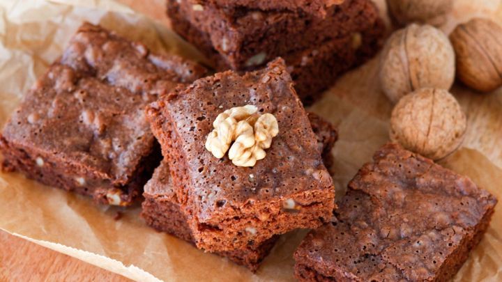 Saftige amerikanische Brownies liegen auf braunem Papier, umgeben von Waln&uuml;ssen auf einem Holzbrett.