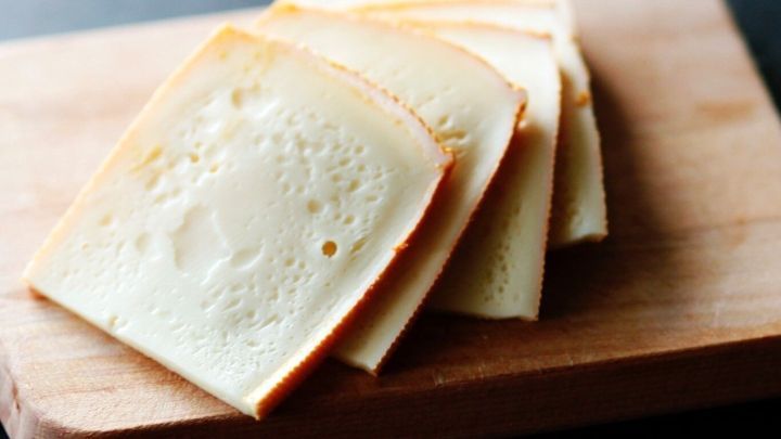 Auf einem Holzbrett liegt frisch geschnittener K&auml;se, der ordentlich in Scheiben angeordnet ist.