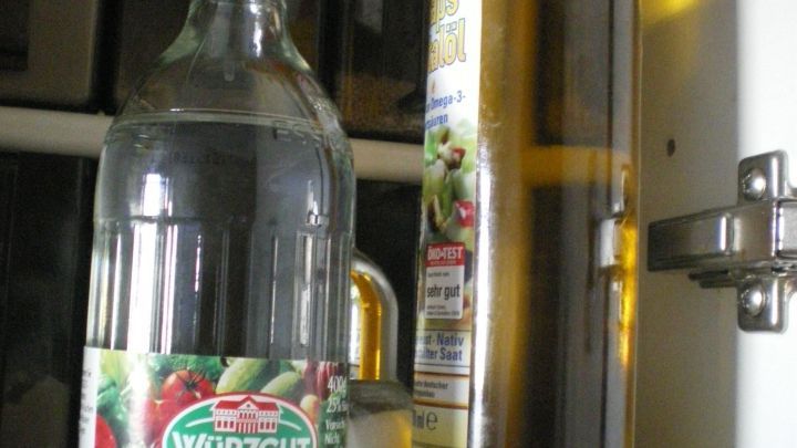 Zwei Flaschen, eine Essigflasche und eine &Ouml;lflasche, stehen auf bunten Untersetzern im K&uuml;chenschrank.