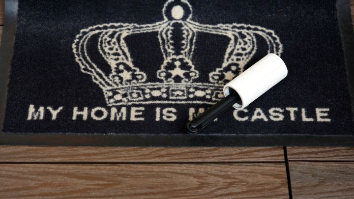 Auf einer dunklen Fu&szlig;matte mit einer Krone liegt eine Fusselrolle, bereit, die Teppichunterlage zu reinigen.