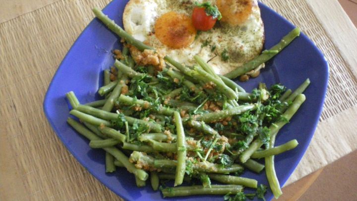 Ein blauer Teller pr&auml;sentiert eine einfache Mahlzeit aus Resten mit gebratenem Ei und gr&uuml;nem Gem&uuml;se, auf einem Tisch.